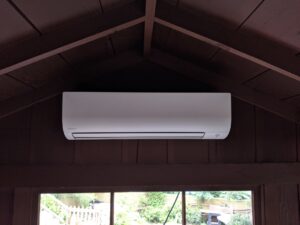 White wall-mounted mini split air conditioner mounted on a dark wall above a large window.