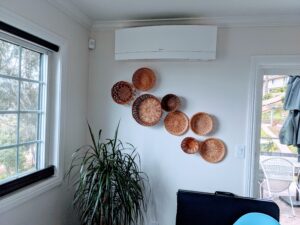 White Mini Split Air Conditioner inside unit installed above baskets collection neaar window in a living room in San Diego.