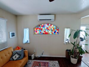 White wall-mounted Daikin Mini Split Air Conditioner inside unit installed by Accord Air in San Diego above a stained-glass window in the stuffed living room.